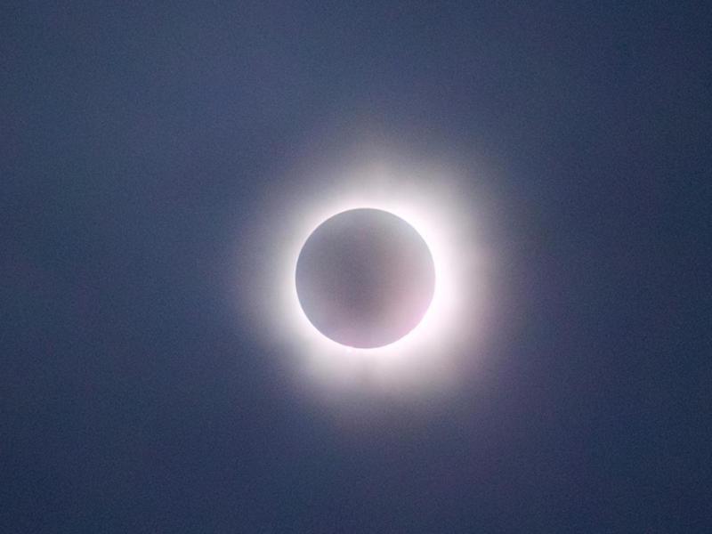 The image captures a solar eclipse in its totality phase, where the moon completely covers the sun, leaving only the bright corona visible as a glowing ring around the darkened disk. The sky appears dark, adding to the dramatic effect of the eclipse. The soft, glowing light of the corona creates a striking contrast against the shadowed moon, making this a captivating depiction of a natural celestial event.