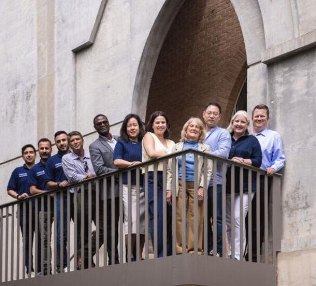 The Bill Munday School of Business faculty and staff stand outside Trustee Hall on the stairway patio.