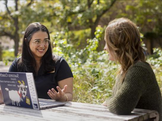 A student meets with a success coach at a patio table.