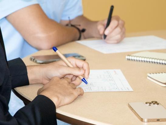 Two students take notes at a table.